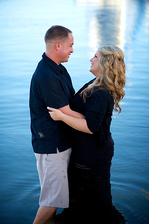 A couple stands in blue water, embracing each other and looking into each other's eyes.