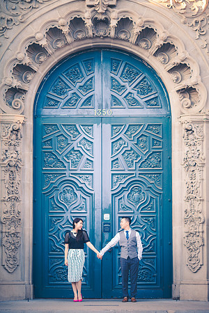 A couple stands together in front of  the entrance to San Diego's Museum of Man; a huge, ornately decorated blue door with an ornamental stone archway above it.