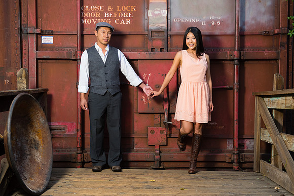 Man and woman dressed in nostalgic outfits holding hands in front of a large metal door on a vintage train car at a location in Old Poway Park near Poway, California.