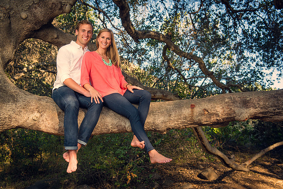 Engagement couple in jeans with bare feet sitting on a tree branch in a wooded area of Mission Trails Park
